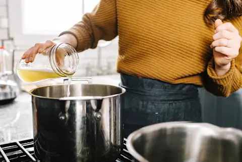   Kvinde hælder bouillon i en gryde på komfuret