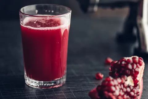 Glas granatæblejuice med saftpresser i baggrunden og en skive af frugten
