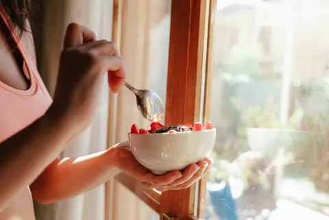 fiatal nő sport melltartó eszik reggeli tál gyümölcs joghurt magvak és csokoládé