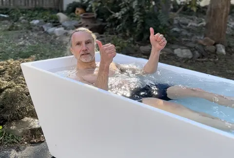   Tester sidder i det kolde springbad med tommelfingeren op i sin hjemmehave