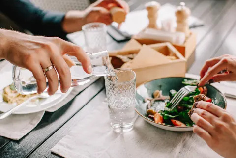   Mand, der hælder et glas vand under frokosten på en restaurant