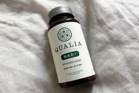 زجاجة Qualia NAD+ على غطاء سرير من الكتان في الغرفة