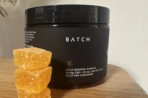 Batch CBD Gold Reserve Gummies på træoverfladen ved siden af tre orange gummier stablet