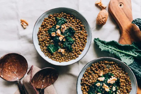 Stilleven van kommen linzen met boerenkool en walnoten op keukentafelkleed/linnen