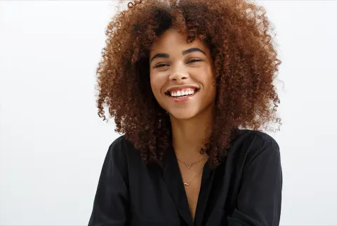 Sort kvinde med krøllet brunette hår, smilende mod en hvid baggrund.