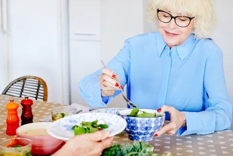   امرأة أكبر سنا تجلس على الطاولة تأكل Salad