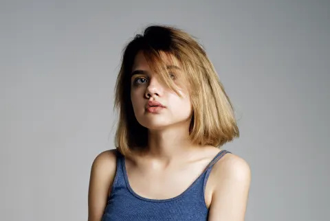   Portræt af smuk teenagepige i blå crop top og grå nederdel, der omfavner sig selv med hånden og ser på kameraet