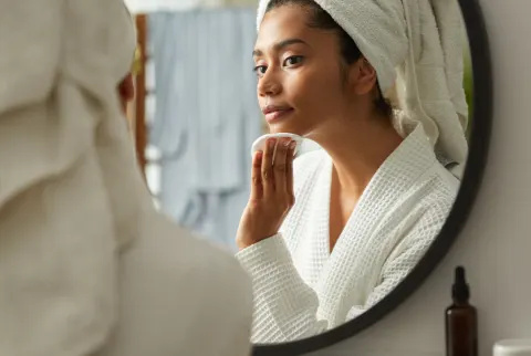 Kvinde på badeværelset fjerner sin makeup, mens hun kigger på spejlet i hudplejemorgen derhjemme