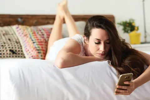   Smuk brunette pige, der bruger mobiltelefon på sengen.