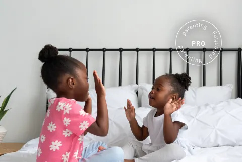   Små piger, der sidder på en seng og spiller Patty Cake - Pro Parenting